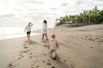 Toddler walks ahead of parents on beach, symbolizing early independence, body tracking, and...