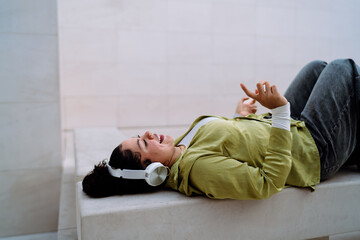 Woman enjoying immersive music experience with wireless headphones, lying down and feeling the...