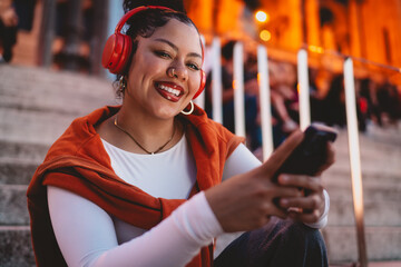 young happy Hispanic woman enjoys music through wireless headphones while browsing her smartphone....