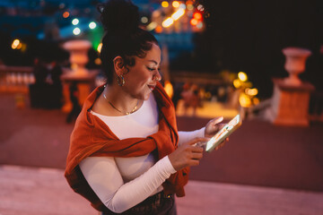 smiling woman enjoys digital experience on her smartphone at night. City lights reflect in her eyes...