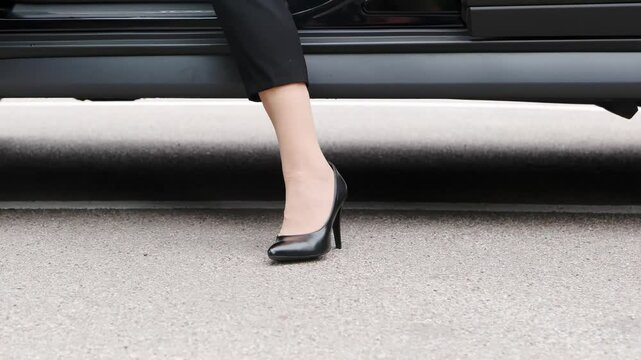 Elegant woman stepping out of sleek black car on asphalt during modern carwash experience outdoors