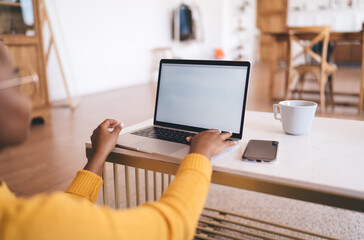 Over-shoulder view of African woman with laptop on white table, hand on keyboard, blank screen...
