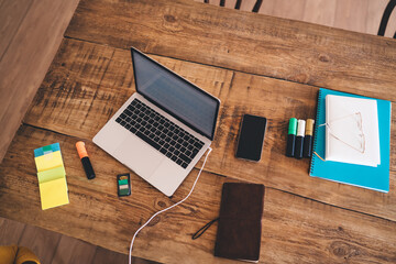 Flat lay of tidy wooden desk setup with closed laptop, colorful markers, sticky notes, smartphone...