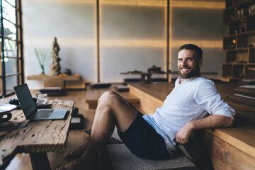Smiling freelancer reclining in relaxed posture beside laptop, portraying harmony between...