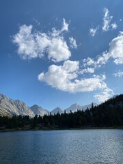 Peaceful lake nestled among mountains under a bright blue sky with fluffy clouds in the early afternoon of a summer day