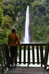Girl stands on a wooden platform and admires the tall, impressive Thunder Creek Falls in Mount...