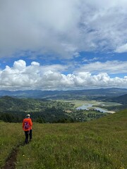 Obraz premium Hiker explores a scenic mountain trail under a cloudy sky in the afternoon, surrounded by lush green hills and a vast valley