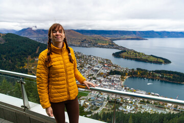 Girl smiling and enjoying panoramic views of Queenstown city, Lake Wakatipu, and surrounding...