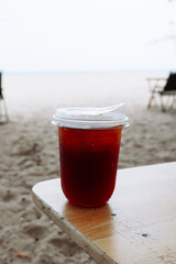 Soft Drink at beach, coffee with ice and straw in plastic glass at beach, Close up of take away plastic cup of iced black coffee (Americano) with drop, Black coffee in a plastic cup on the beach