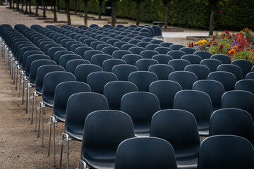 Multiple rows of identical black chairs are neatly arranged in an outdoor setting on a dirt surface, creating a uniform and symmetrical pattern.