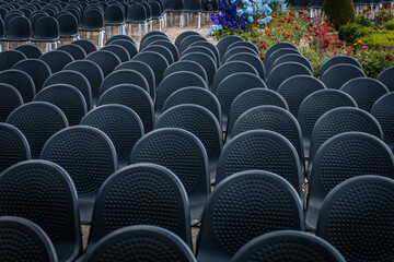 Multiple rows of identical black chairs are neatly arranged in an outdoor setting on a dirt...