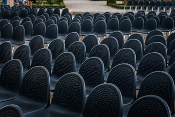 Obraz premium Multiple rows of identical black chairs are neatly arranged in an outdoor setting on a dirt surface, creating a uniform and symmetrical pattern.