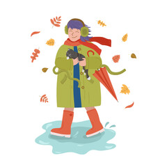 Girl in headphones and an umbrella walks with a kitten. Autumn, leaf fall. Rubber boots, puddles. Girl in a coat and fur headphones. Warm clothes, cold season. Adopt animals.