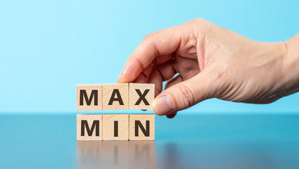 A hand places a wooden block with the word max on top of min, representing extremes or limits