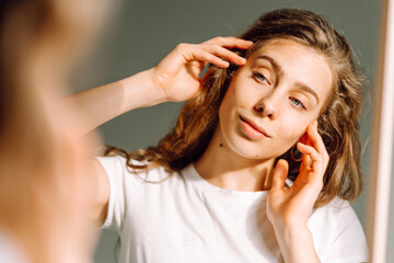 Close-up face of a young woman with rashes looking at the mirror in a cozy room. Beautiful woman...