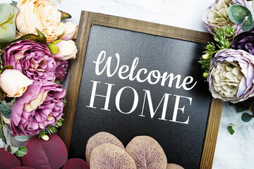 Welcome Home text on blackboard with flowers decoration on marble background