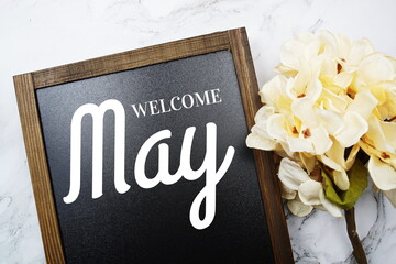 Welcome May text on blackboard with flowers decoration on marble background