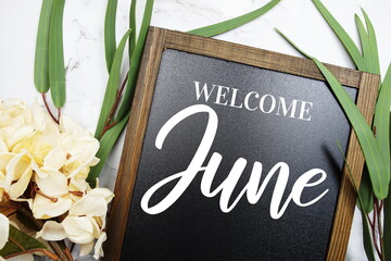 Welcome June text on blackboard with flowers decorated on marble background