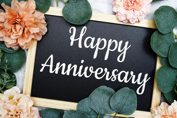 Happy Anniversary text on blackboard with flowers decorated on marble background