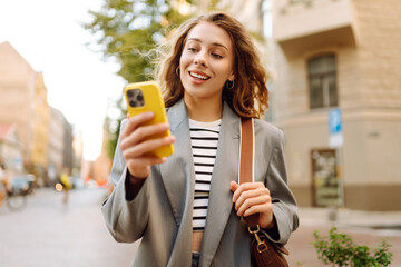 Portrait of a happy woman with a phone in her hands walking along the streets of the city. A...