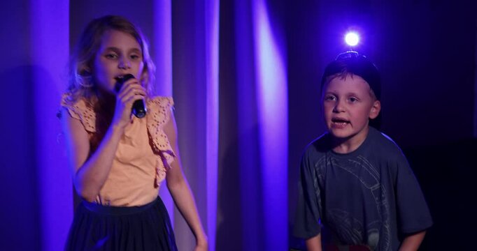 energetic kids stage concert performance at home. boy playing cardboard guitar and girl sing in the microphone. neon lighting
