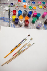 Brushes on a white sheet of paper and jars of multi-colored paint for drawing on the table