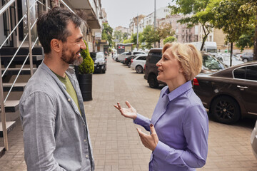 Lively discussion occurs outside as adult male with a hearing aid joyfully connects with woman...