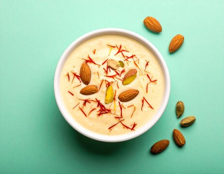 Creamy basundi with saffron and almond garnish in bowl on mint green background &mdash; smooth Indian milk dessert