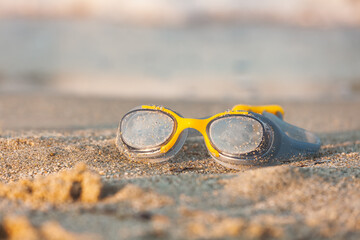 Swimming goggles on beach sand in golden sunset light
