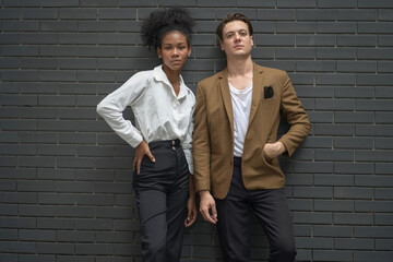 Confident young man and woman in smart casual attire standing against a modern dark brick wall