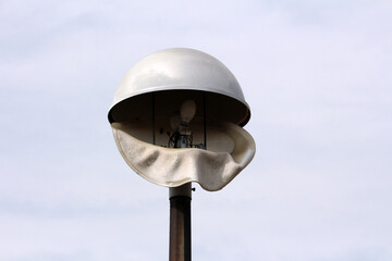 A street lamp features a white dome shade warped and melted, exposing bulbs and wiring,...