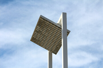 A tall, white solar-powered streetlight features a large, square grid of solar panels angled toward the sky, showcasing sustainable urban lighting technology against a blue sky