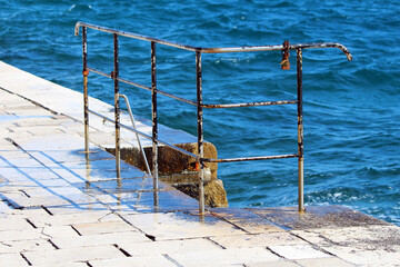 A weathered metal railing with visible rust and a padlock stands on a wet stone pier, leading to a...