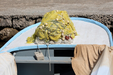 A tangled yellow fishing net with white and brown floats is heaped on the bow of a light blue...