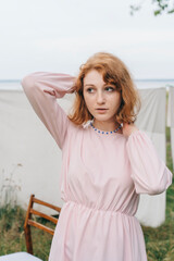 Red-haired woman in pink dress wearing blue beaded necklace outdoors