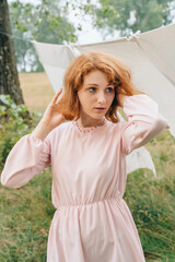 Naklejka premium Red-haired Woman in Pink Dress Outdoors with Linen Background