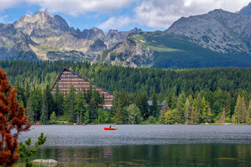 Scenic summer view of Strbské Pleso in the High Tatras, Slovakia. Tourists enjoy peaceful boat rides on the crystal-clear mountain lake, surrounded by a lush green forest