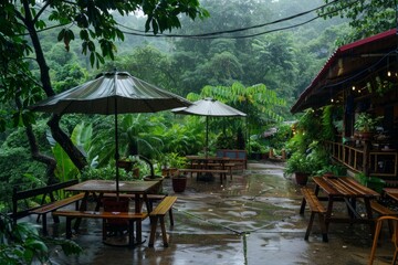 Wooden tables and benches getting wet under umbrellas on a rainy day in a tropical forest restaurant