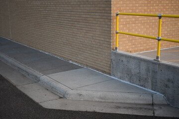 Sidewalk ending at brick building. Yellow metal railing.