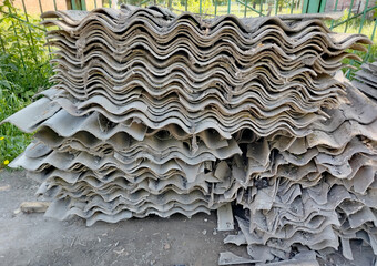 Old gray slate, stacked in uneven piles and broken into pieces of different shapes and sizes. Construction waste after roof repair