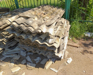Old gray slate, stacked in uneven piles and broken into pieces of different shapes and sizes. Construction waste after roof repair