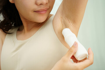 Asian young woman applying roll on deodorant reduce underarm sweat and odor after shower.