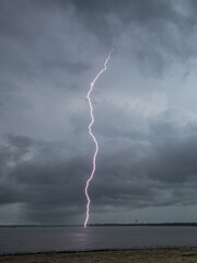 Lightning strikes over the calm water under a cloudy sky during a summer storm in the late afternoon