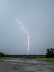 Lightning strikes over the calm water under a cloudy sky during a summer storm in the late afternoon