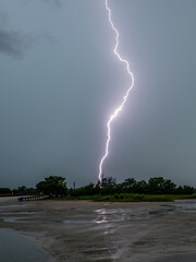 Lightning strikes over the calm water under a cloudy sky during a summer storm in the late afternoon
