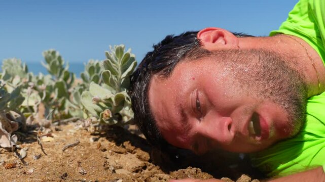 a wet man lies exhausted on the sand and scoops sand into his hand