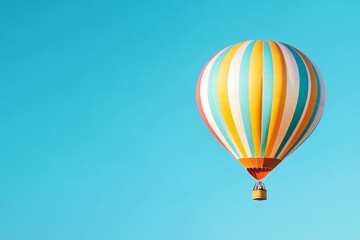 Fototapeta premium Colorful Hot Air Balloon Soaring High - A vibrant hot air balloon with orange, yellow, white, and teal stripes floats against a clear blue sky. Perfect for travel, adventure, and freedom themes