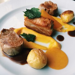 Elegant Western gourmet dish: seared meat medallions, crispy pork belly, roasted potatoes, vibrant carrot puree, rich demi - glace, and fresh mint, artfully plated on white ceramic.