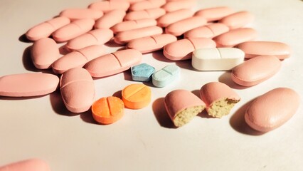 A collection of various pills and medications, including pink, yellow, blue, and white tablets, scattered on a white background, representing health and pharmaceuticals.