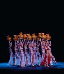Belly dancers are elegantly holding vases while performing on a stage